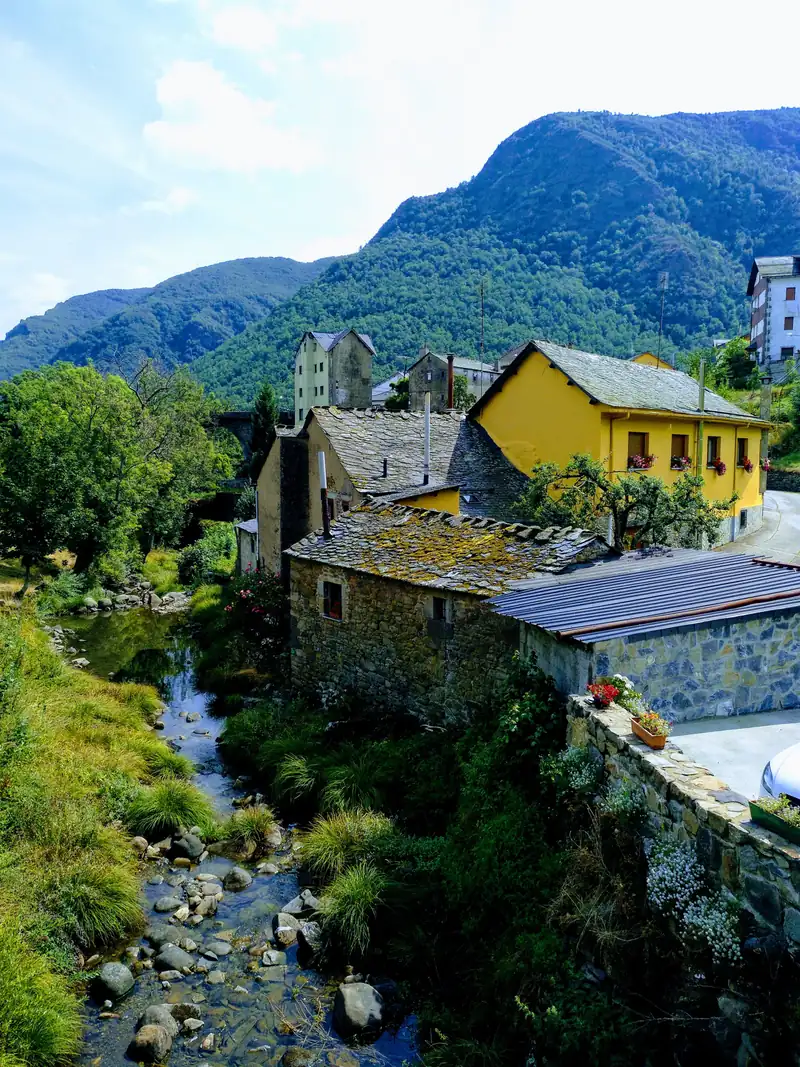Casas de piedra con tejados de pizarra junto al río, en Caboalles de Abajo (Laciana), con la montaña verde al fondo