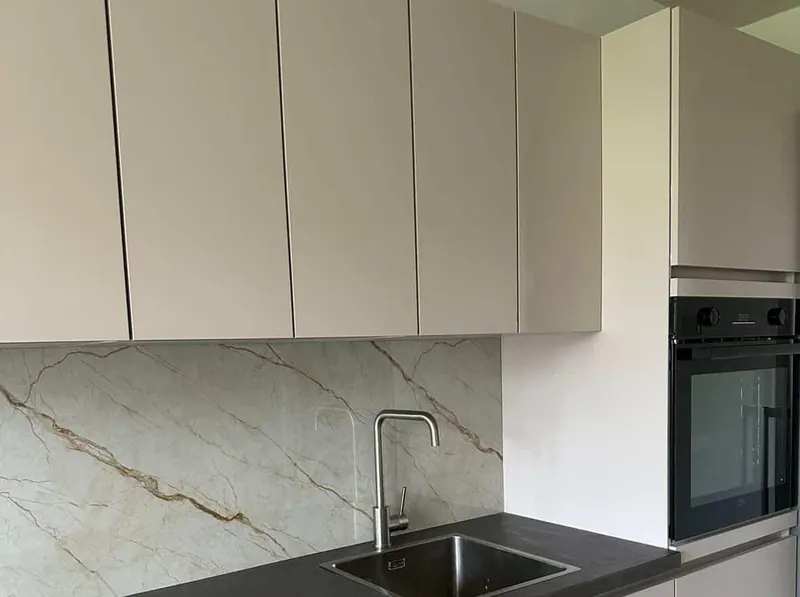Cocina con muebles lisos claros, encimera oscura y un salpicadero de una sola pieza con vetas doradas